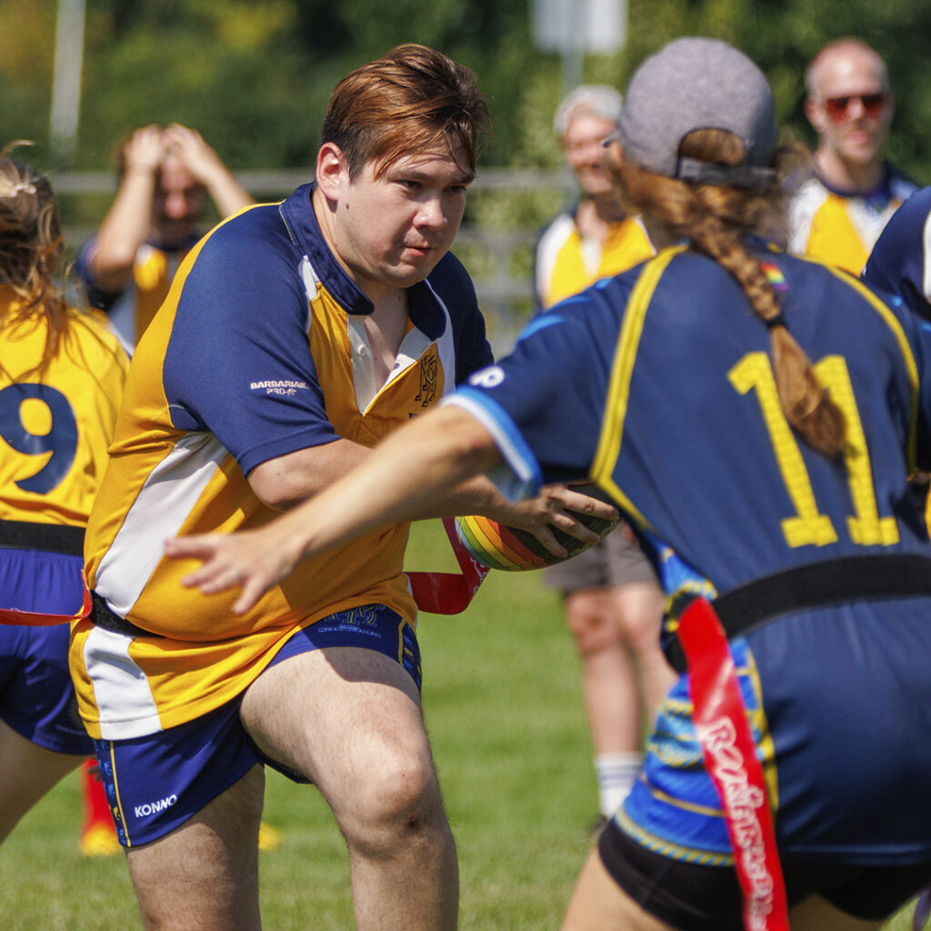 Muddy York player running forward during a flag game. He is trying to avoid having his flag pulled.