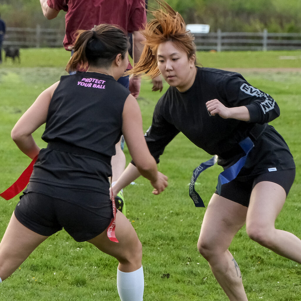 Two teammates playing a flag rugby drill. One has blue flags and is trying to keep hers away from the other wearing red flags.